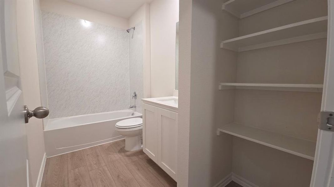 Full bathroom featuring a white tub, shower with a textured surround, single vanity with white cabinetry, and wood-finish flooring Full bathroom featuring a white tub, shower with a textured surround, single vanity with white cabinetry, and wood-finish flooring