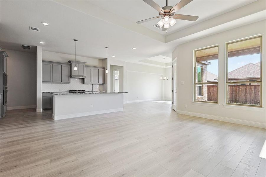 Kitchen featuring decorative backsplash, an island with sink, hanging light fixtures, gray cabinetry, and light hardwood / wood-style floors