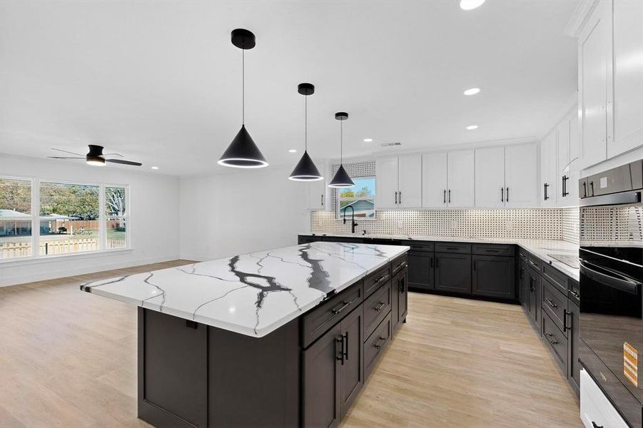 Kitchen featuring white cabinetry, decorative backsplash, hanging light fixtures, light stone counters, and dark cabinets