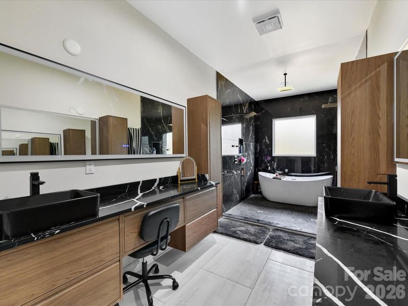 Luxurious primary bathroom featuring dual vanities, sleek modern finishes, a soaking tub, and a spacious walk-in shower with dramatic tile accents.