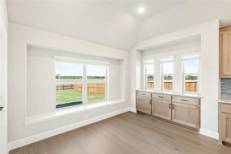 Bright dining area with large windows, light wood floors, and built-in cabinetry overlooking a fenced backyard Bright dining area with large windows, light wood floors, and built-in cabinetry overlooking a fenced backyard