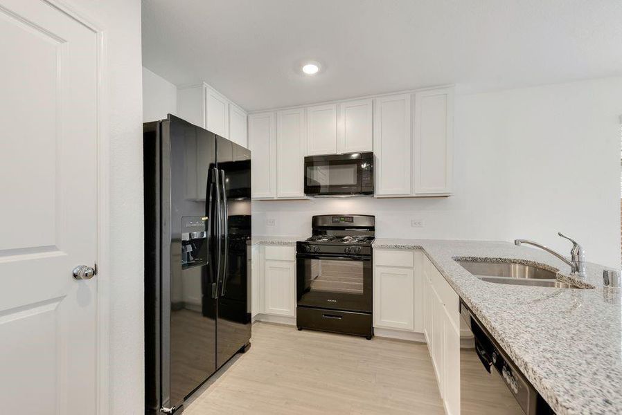 Kitchen with black appliances, a sink, light stone countertops, and white cabinets