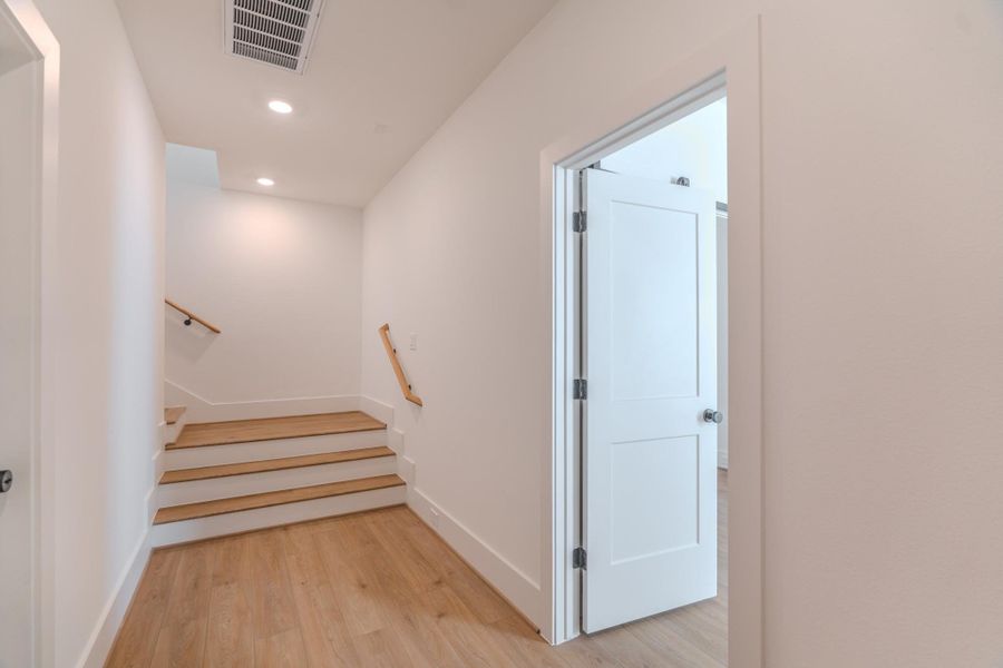 This photo features a bright, modern hallway with light wood flooring and a staircase leading upward. A white door on the right opens into another room, enhancing the airy and spacious feel.Photo Disclaimer: Photos are representative of the community and may depict a similar floor plan, model home, or previously completed residence. This photo features a bright, modern hallway with light wood flooring and a staircase leading upward. A white door on the right opens into another room, enhancing the airy and spacious feel.Photo Disclaimer: Photos are representative of the community and may depict a similar floor plan, model home, or previously completed residence.