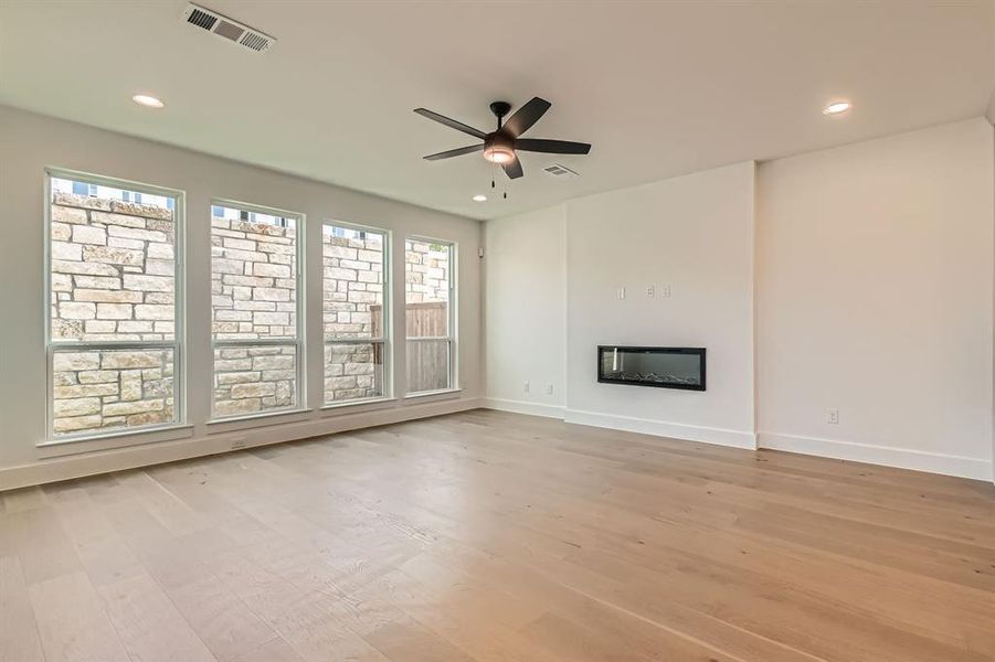 Unfurnished living room with light wood-style floors, a ceiling fan, baseboards, recessed lighting, and a glass covered fireplace
