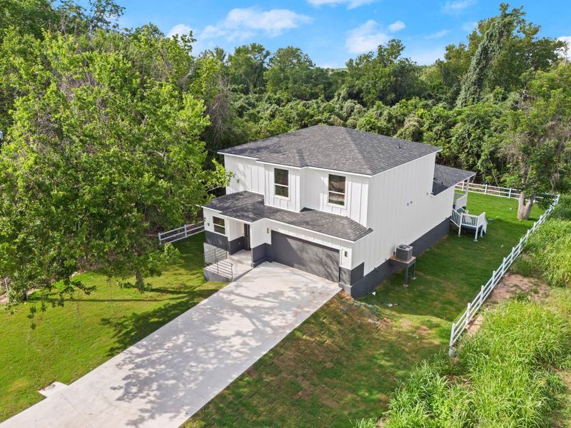 View of front of house with a shingled roof, a garage, concrete driveway, and a forest view