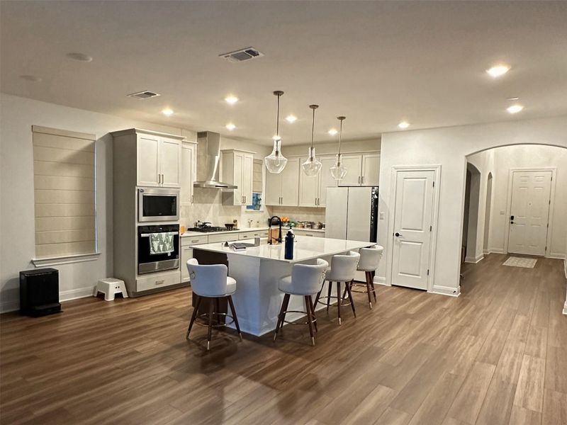 Open-concept kitchen featuring an oversized island with seating, pendant lighting, stainless steel appliances, and light wood-finish flooring Open-concept kitchen featuring an oversized island with seating, pendant lighting, stainless steel appliances, and light wood-finish flooring