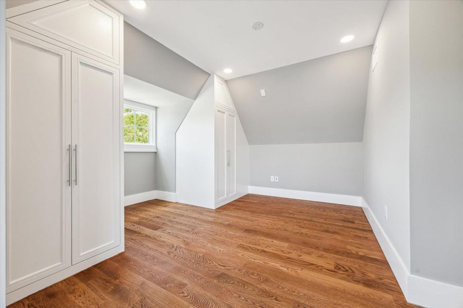 Another view of this 3rd floor modern yet cozy bedroom that features hardwood floors, sloped ceilings, and built-in storage. Windows allows natural light to fill the space, creating a warm and inviting atmosphere.
