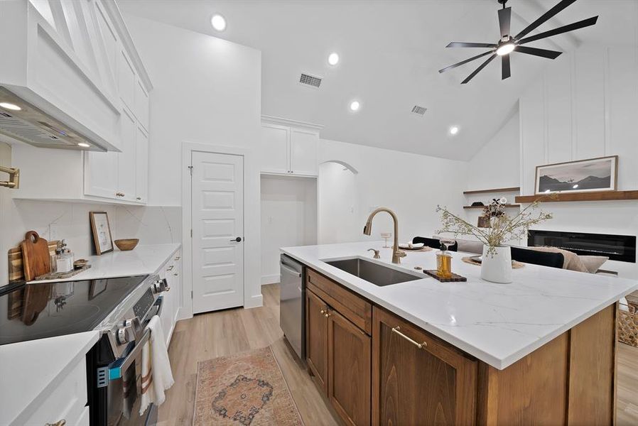 Open-concept kitchen featuring an island with a stainless steel undermount sink, a gold-tone faucet, and white countertops Open-concept kitchen featuring an island with a stainless steel undermount sink, a gold-tone faucet, and white countertops