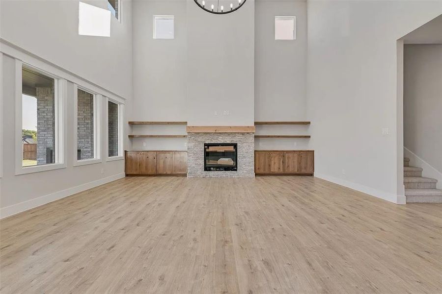 Unfurnished living room with light wood-type flooring, a fireplace, hanging lights, and a high ceiling