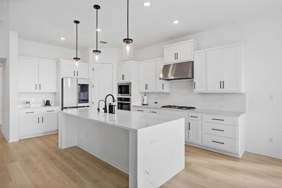 Kitchen with pendant lighting, light stone countertops, light wood-style flooring, decorative backsplash, and appliances with stainless steel finishes