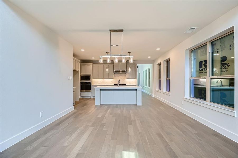 Kitchen with light countertops, light wood-style floors, backsplash, appliances with stainless steel finishes, and decorative light fixtures