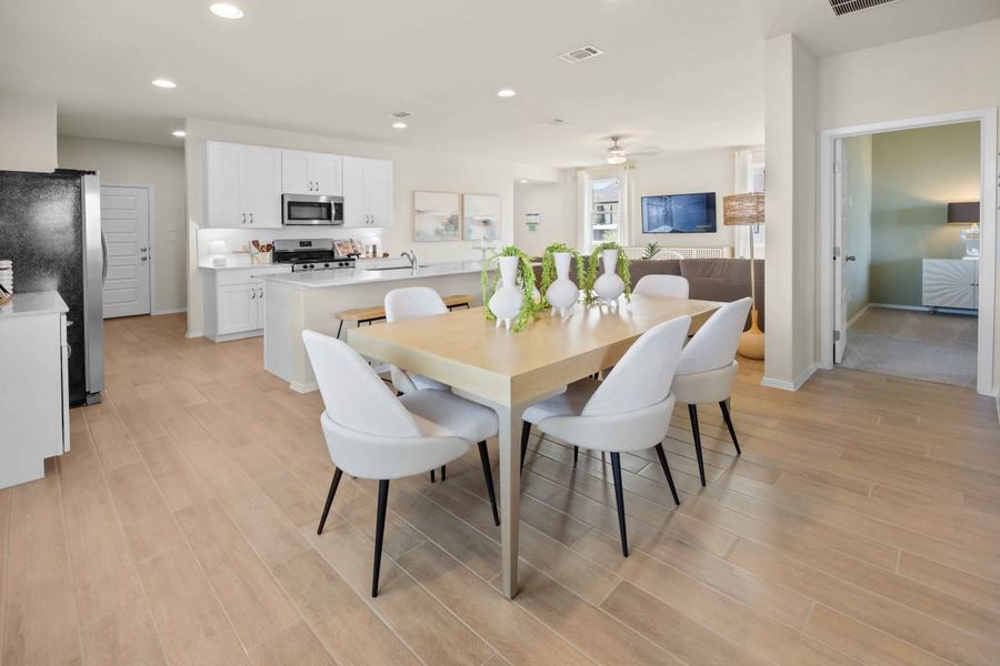 An interior image of a tan dining table view of the kitchen with vinyl flooring, white cabinets and countertop.