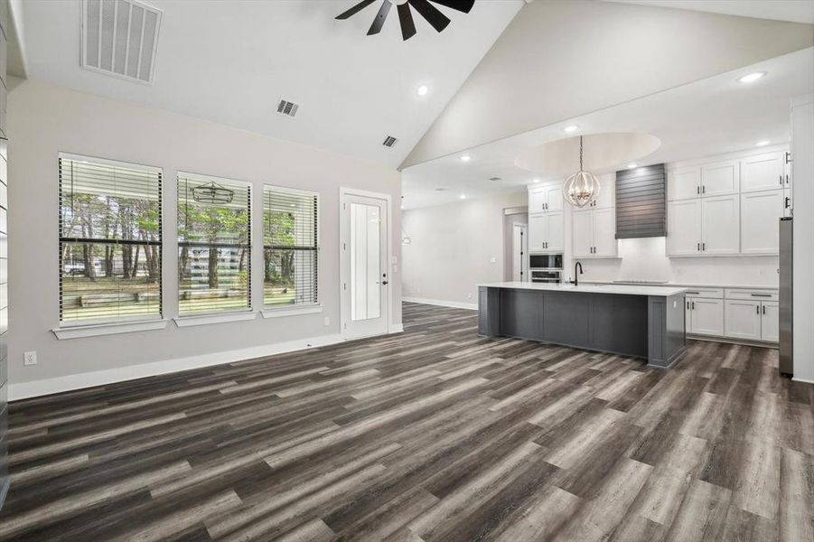 Kitchen with ceiling fan with notable chandelier, white cabinets, an island with sink, high vaulted ceiling, and dark hardwood / wood-style floors