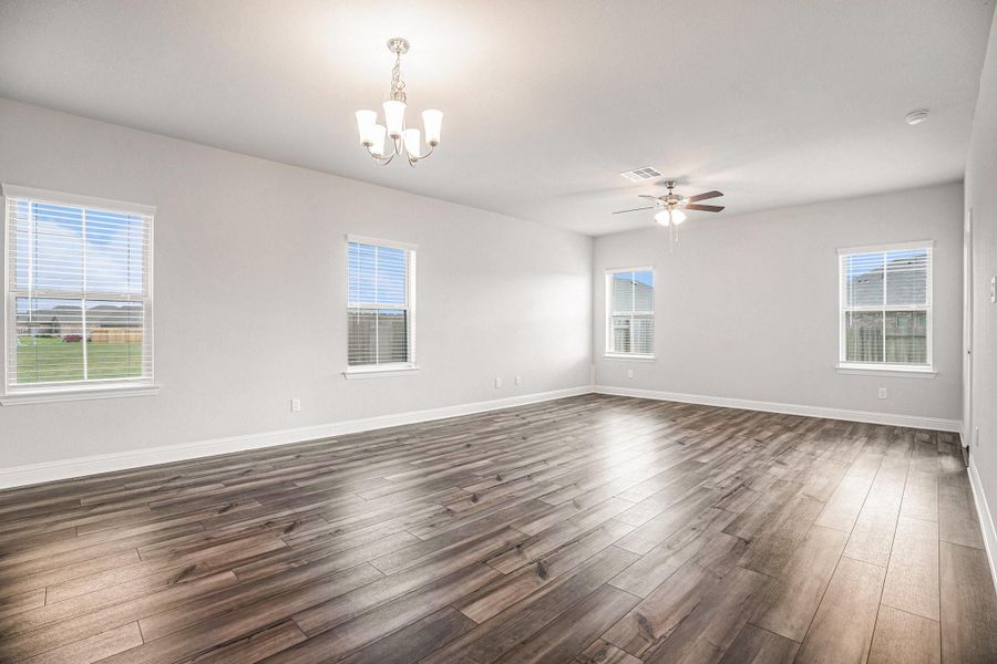 This spacious living area features luxury vinyl plank flooring, ample natural light from multiple windows, a modern ceiling fan, and a stylish overhead light fixture, creating a warm and inviting atmosphere.