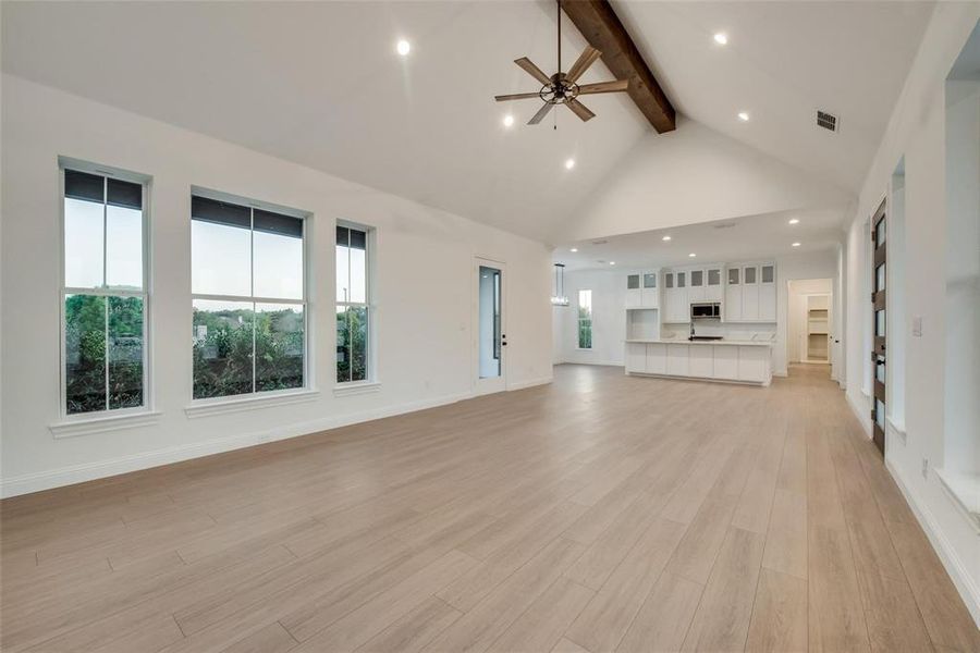 Unfurnished living room with beamed ceiling, recessed lighting, high vaulted ceiling, light wood-style floors, and ceiling fan