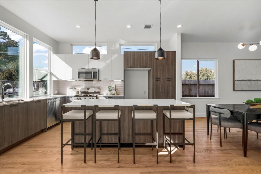 Sunlit kitchen featuring two-tone European-style cabinetry, quartz countertops & stainless steel appliances, designed with a large island perfect for dining & entertaining. Sunlit kitchen featuring two-tone European-style cabinetry, quartz countertops & stainless steel appliances, designed with a large island perfect for dining & entertaining.