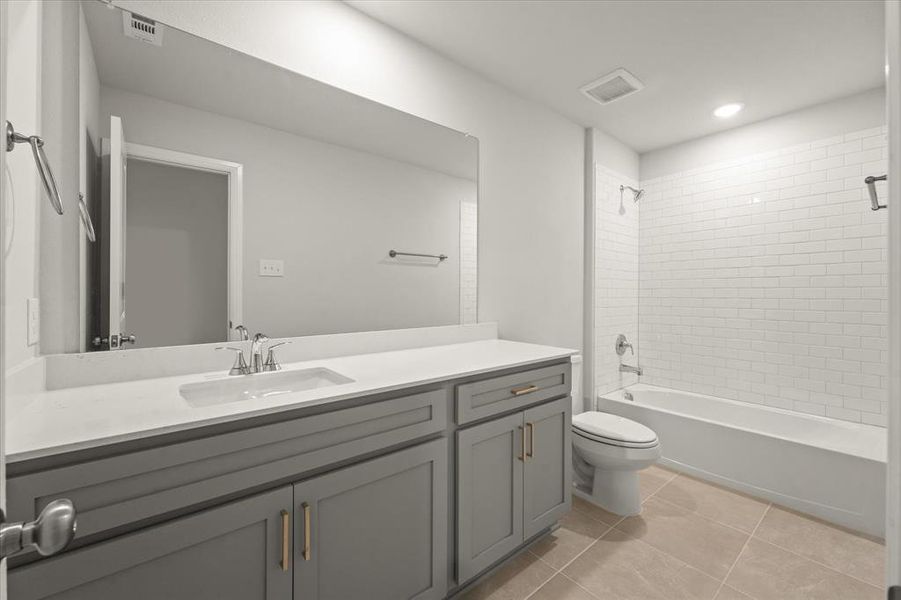 Full bathroom with toilet, vanity, tiled shower / bath, and tile patterned flooring