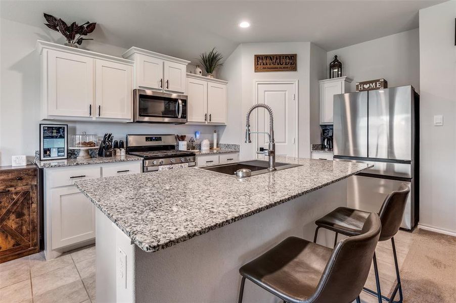 Kitchen featuring stainless steel appliances, light stone counters, white cabinetry, a kitchen breakfast bar, and a kitchen island with sink