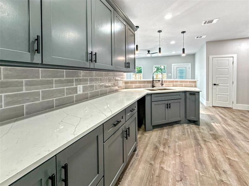 Kitchen with backsplash, gray cabinetry, pendant lighting, light wood-style flooring, and light stone countertops
