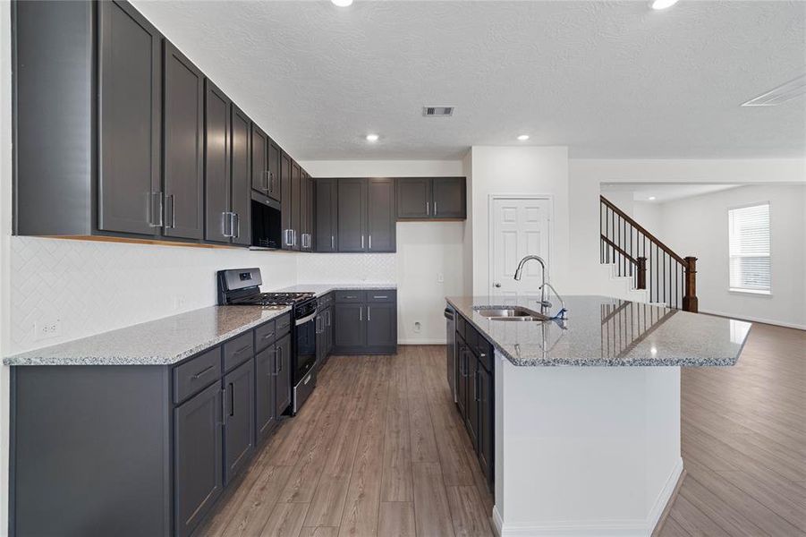 This spacious kitchen features high ceilings, stained wood cabinets, granite countertops, SS appliances, modern tile backsplash, recessed lighting, large kitchen island with space for a breakfast bar, and a pantry all overlooking your huge family room.