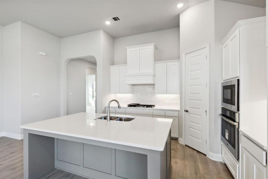 Kitchen with hardwood / wood-style floors, a center island with sink, sink, white cabinetry, and stainless steel appliances