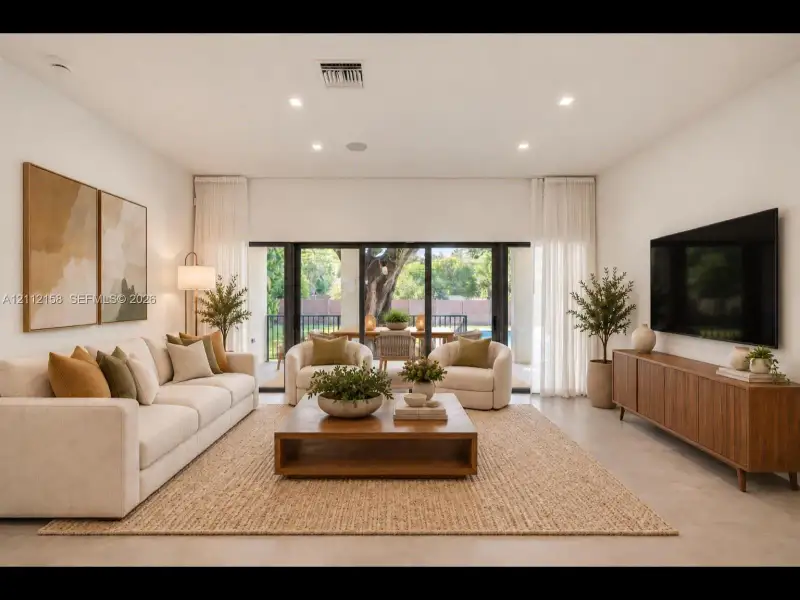 Bright living area with large-format tile, recessed lighting, and multi-panel sliding glass doors that open to the covered patio for seamless indoor-outdoor living