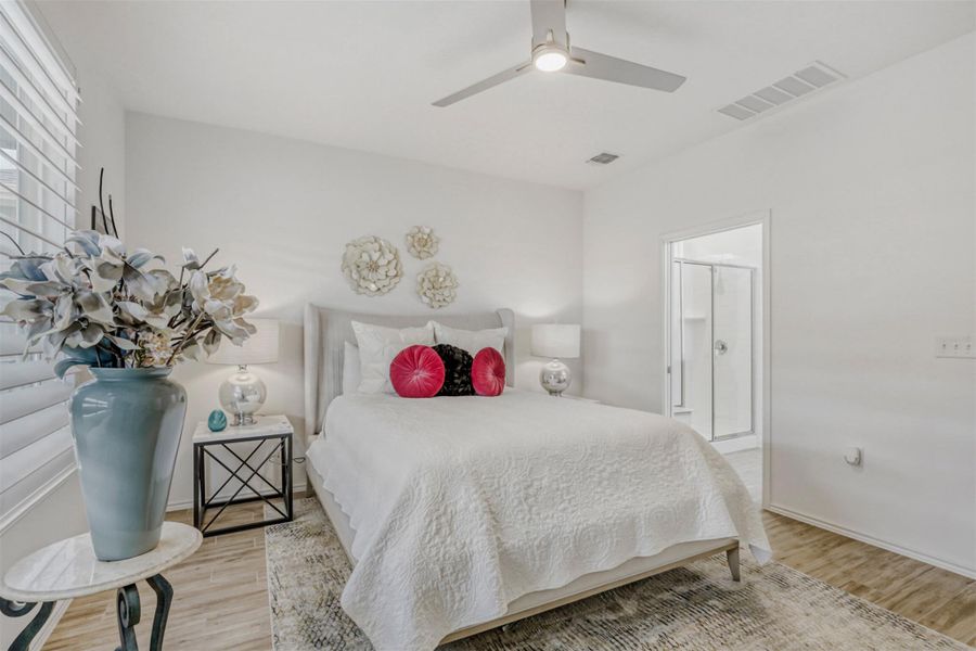 Bedroom with light wood finished floors, ceiling fan, and ensuite bathroom