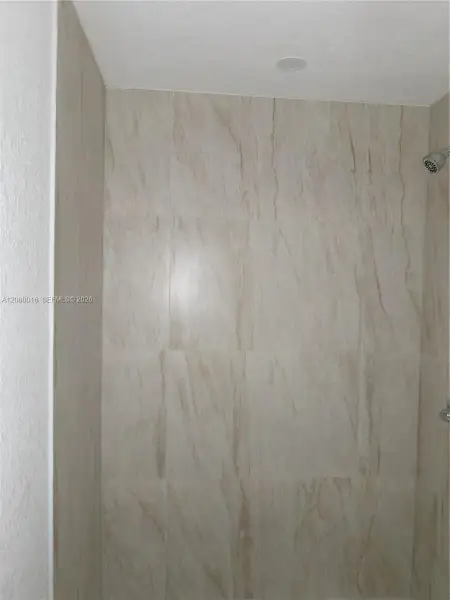 Shower enclosure featuring floor-to-ceiling neutral-toned tile with prominent veining and an integrated recessed ceiling light