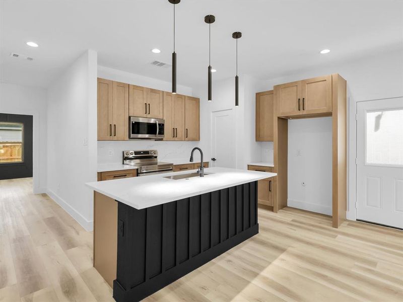 Kitchen with decorative light fixtures, stainless steel appliances, sink, a center island with sink, and light hardwood / wood-style floors