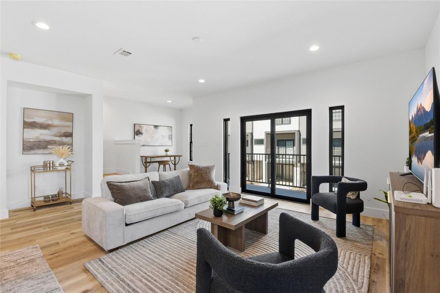 This modern living room features a cozy seating area with a neutral color palette, wood flooring, and large sliding glass doors leading to a balcony.