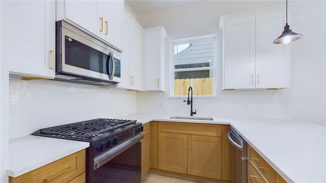 This additional kitchen angle highlights the expansive white countertops and ample cabinetry, offering ideal storage for any chef. A sleek stainless steel farmhouse sink, paired with dark plumbing hardware, adds a modern, sophisticated touch to the space.