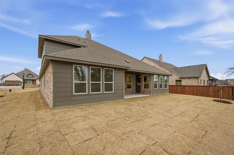 Back of house featuring a patio, a chimney, roof with shingles, and brick siding