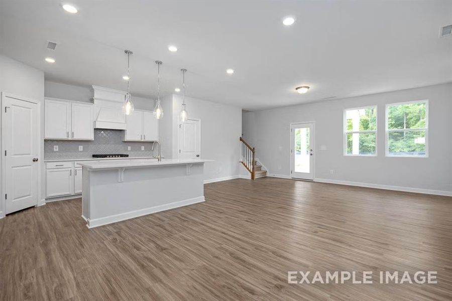 Kitchen with white cabinetry, hanging light fixtures, hardwood / wood-style floors, tasteful backsplash, and a center island with sink