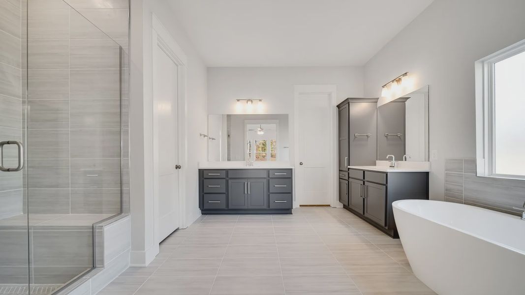 Large tiled bathroom with multiple vanities, glass shower enclosure, and freestanding tub