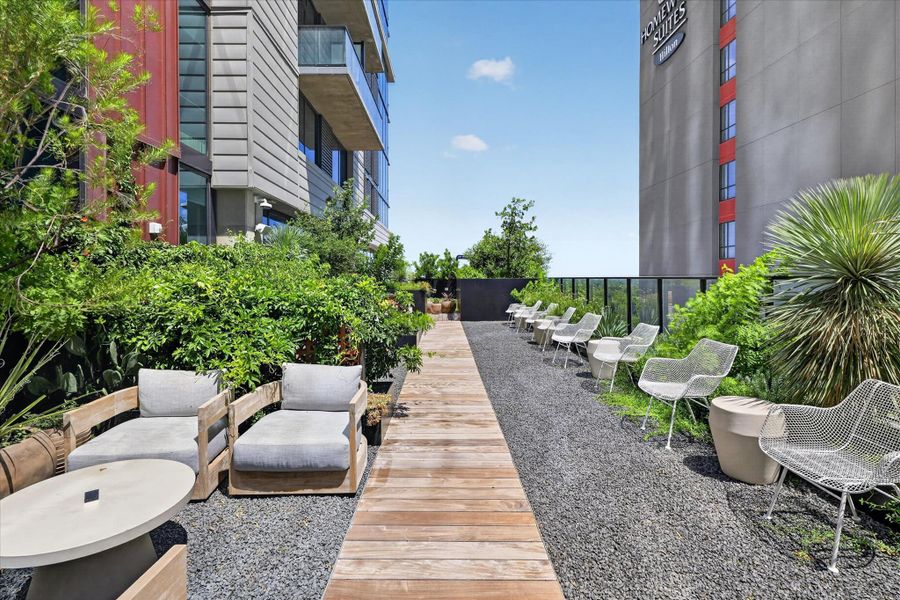 A tranquil rooftop deck, perfect for relaxation, is bordered by lush greenery and offers urban vistas.
