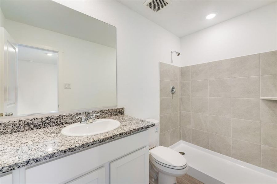 Bathroom featuring a tile shower, vanity, and toilet