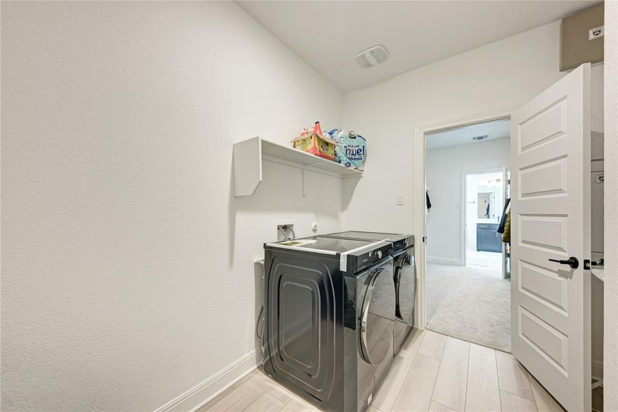 Dedicated laundry area featuring wood-finish flooring, a contemporary white door with matte black hardware, and a built-in wall shelf