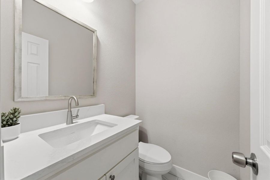 Powder room near foyer features quartz countertops, designer mirror, and elongated commode.