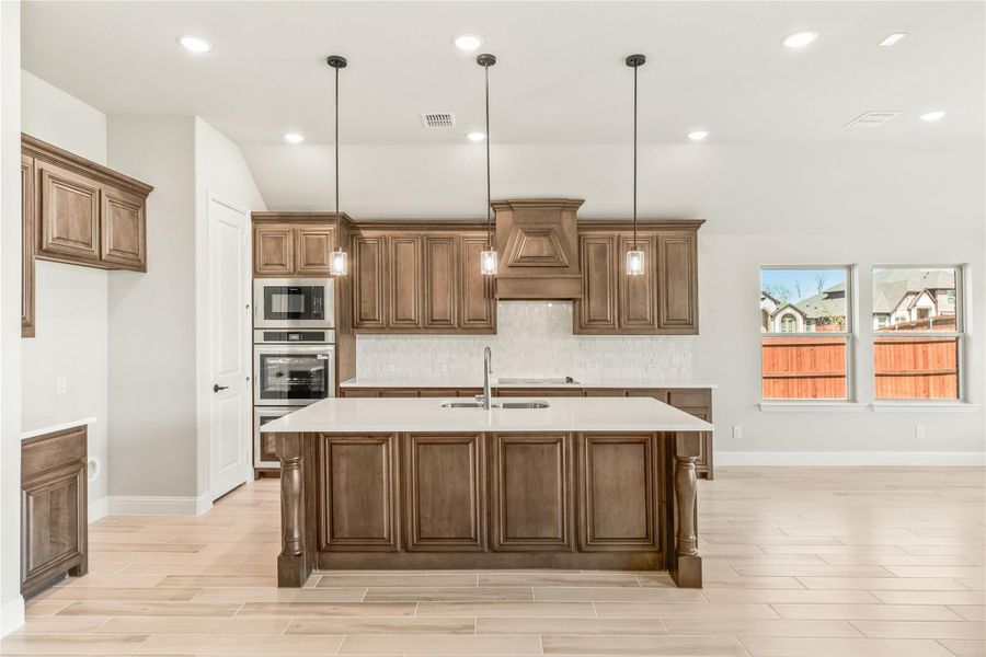 Kitchen with dark wood cabinets, large center island, pendant lights, and double wall ovens on light tile floors Kitchen with dark wood cabinets, large center island, pendant lights, and double wall ovens on light tile floors