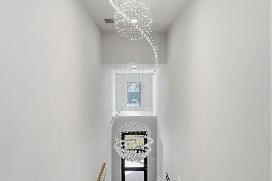 A breathtaking multi-story crystal chandelier creates a dramatic first impression, cascading gracefully through the soaring foyer and serving as a stunning architectural centerpiece visible from both levels of the home.