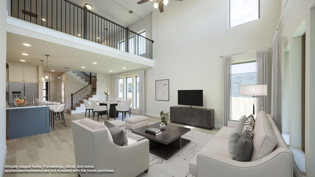Living area with healthy amount of natural light, light wood-type flooring, a towering ceiling, a ceiling fan, and stairway