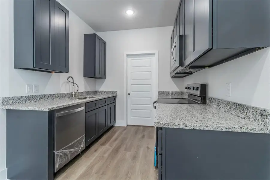 Kitchen featuring stainless steel appliances, sink, light wood-type flooring, light stone countertops, and gray cabinetry
