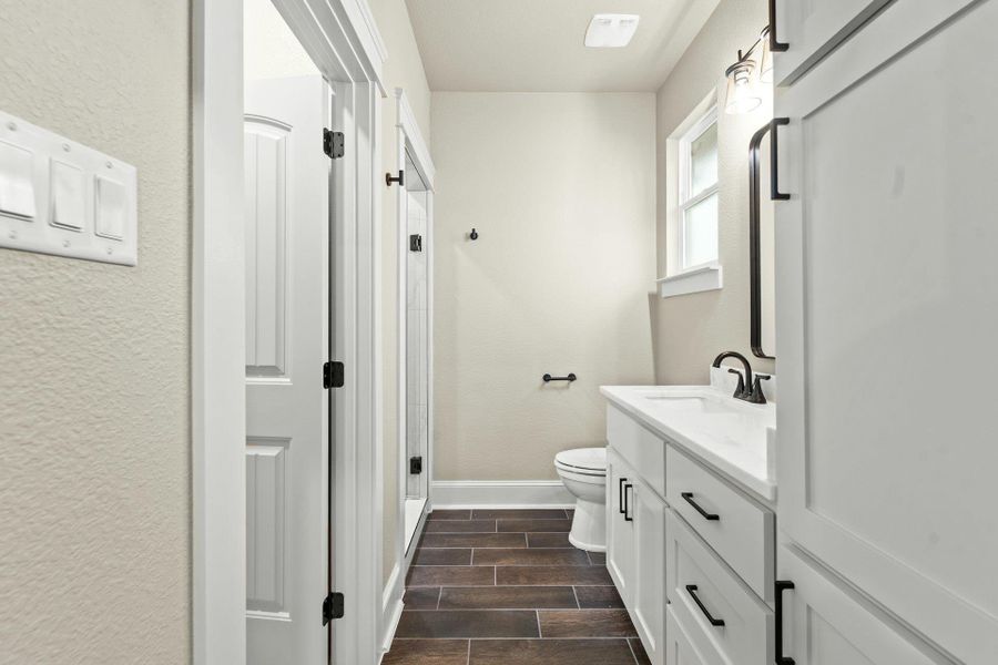Bathroom featuring a white vanity with a light-toned countertop, dark wood-finish flooring, white cabinetry with dark hardware, a window, and a built-in toilet
