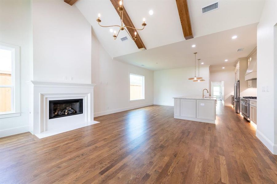 Spacious living area featuring high vaulted ceilings with exposed wood beams, a prominent fireplace with a classic white mantel, and wood-finish flooring Spacious living area featuring high vaulted ceilings with exposed wood beams, a prominent fireplace with a classic white mantel, and wood-finish flooring