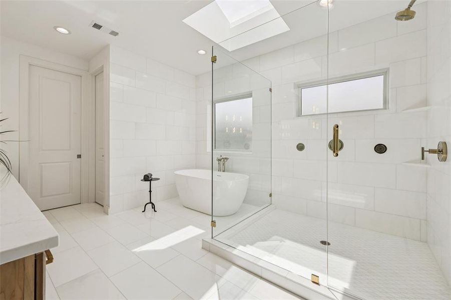 Spacious bathroom featuring a frameless glass shower enclosure, a freestanding soaking tub, and a skylight for natural illumination