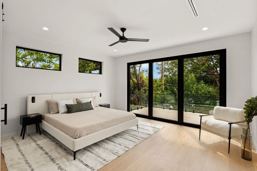 Hardwood floors and sliding glass doors framing leafy views anchor this modern bedroom.