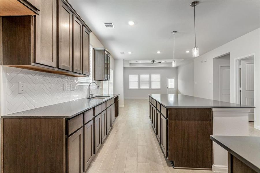 Experience the beauty and functionality of an open floor plan with this spacious kitchen flowing seamlessly into the living area. The modern pendant lighting and high-end finishes create a stylish yet practical space for cooking and entertaining. Large windows and a neutral color palette ensure plenty of natural light throughout the day. Photos are from another Rylan floor plan.