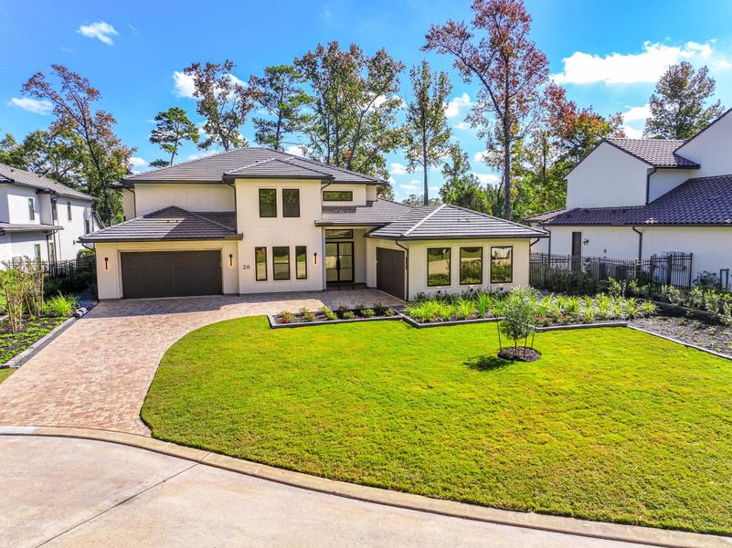 This modern two-story home features a sleek exterior with a spacious driveway and two-car garage. The front yard is beautifully landscaped with a well-maintained lawn and garden beds. Surrounded by tall trees, it offers a sense of privacy and natural beauty.
