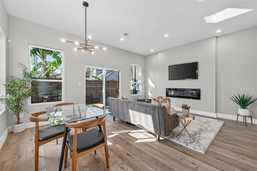 Sunlit living and dining space with seamless indoor-outdoor flow, designer lighting fixtures, and durable, low-maintenance plank laminate flooring with a warm white oak finish.