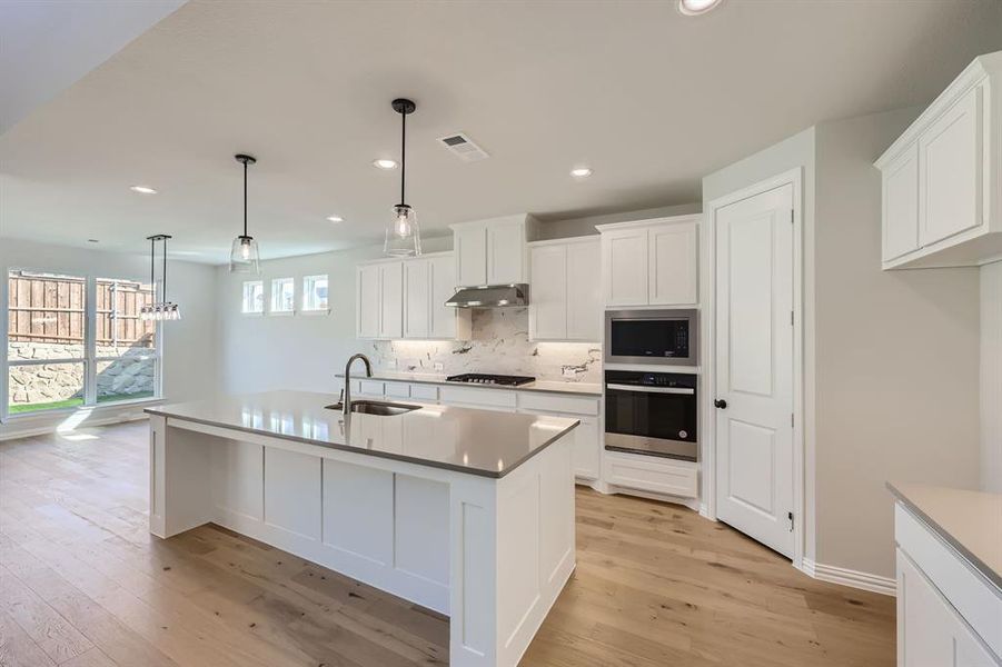 Kitchen featuring appliances with stainless steel finishes, a kitchen island with sink, pendant lighting, light hardwood / wood-style floors, and sink